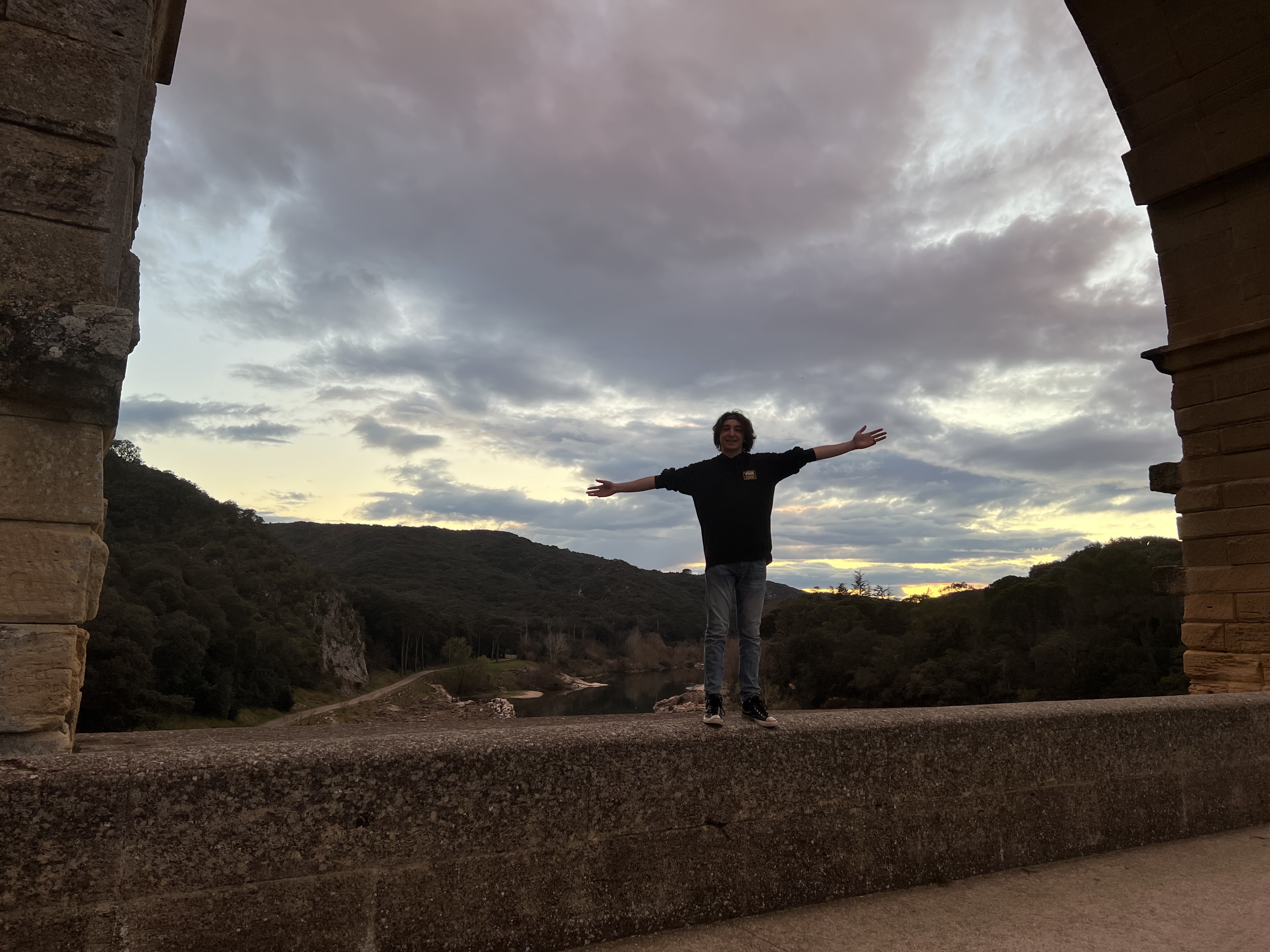 Boyan standing on a part of Pont Du Gard with arms outstretched.