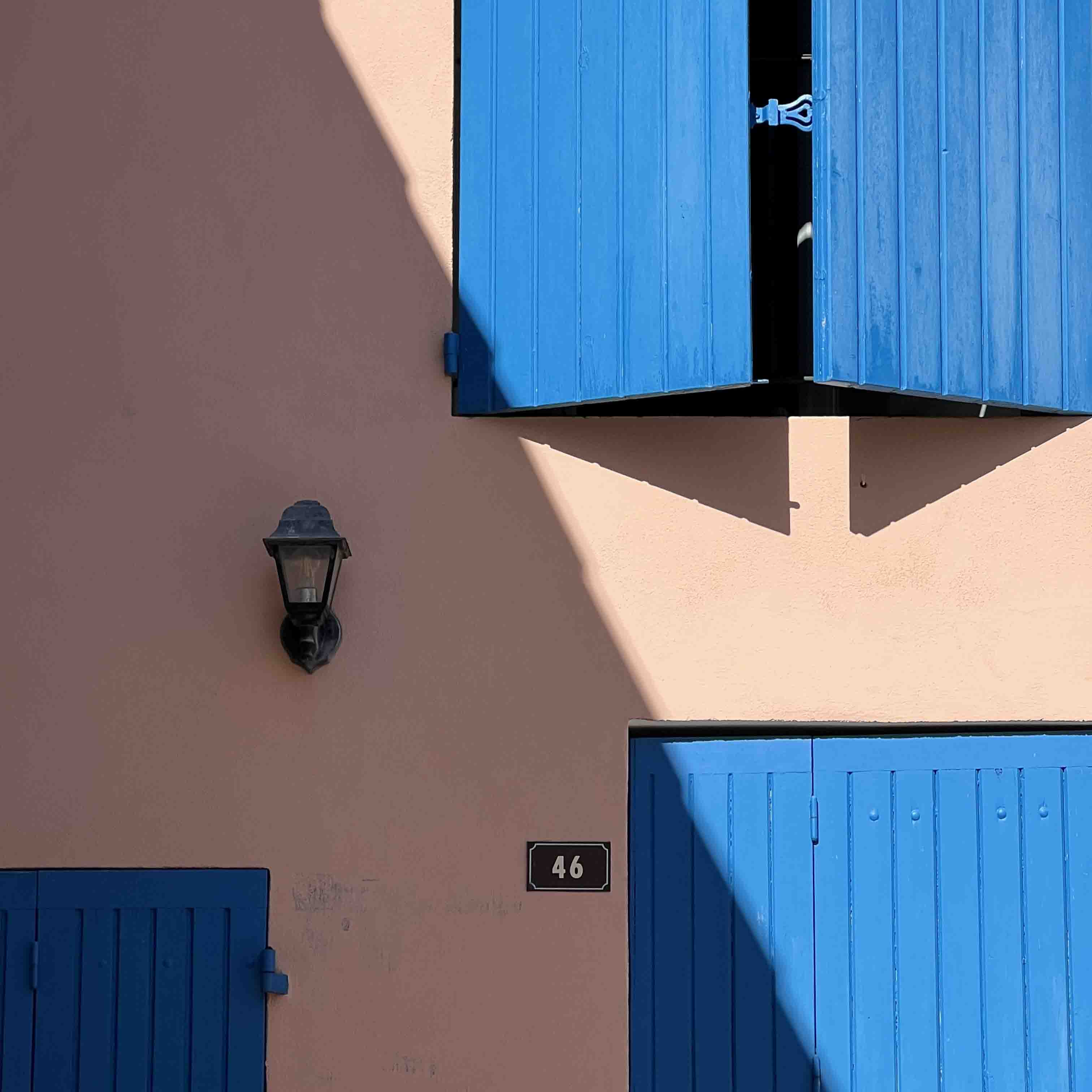 Blue window shutters shadowed by the afternoon sun.