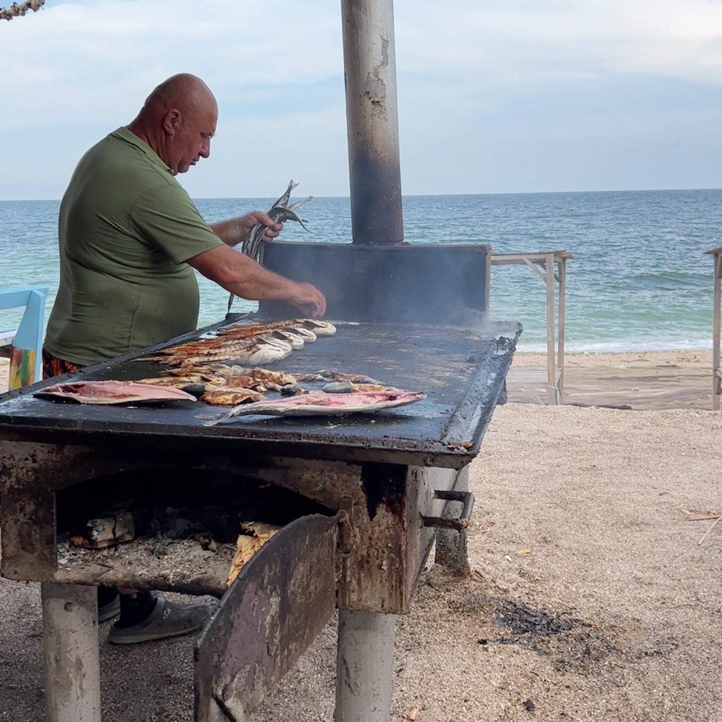 Man frying up fish on the beach on a wood fired flat-top.